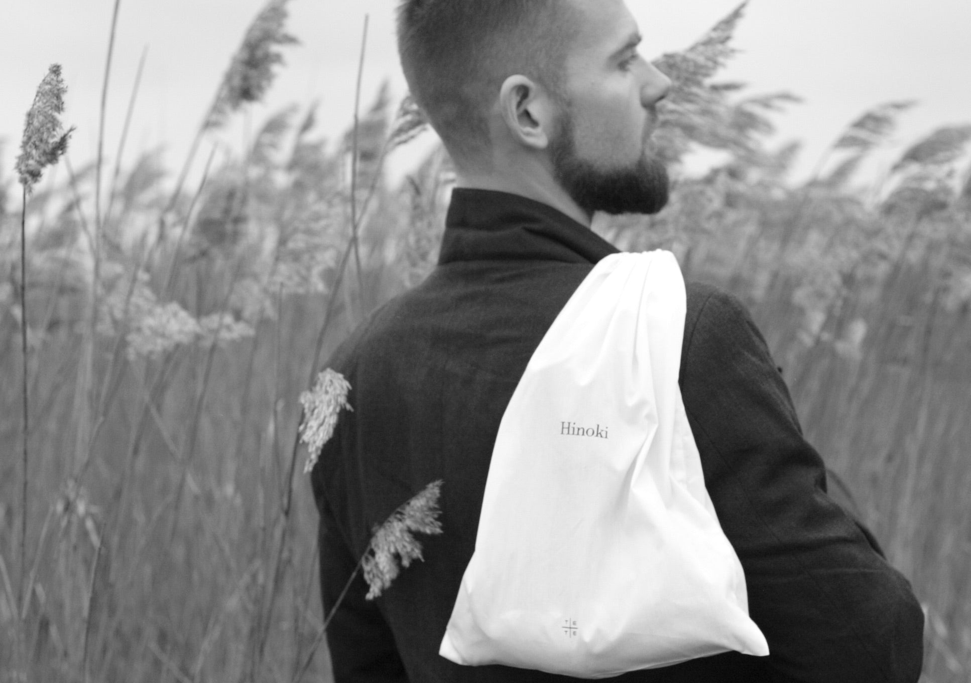 Man wearing a black jacket with a white Hinoki bag over his shoulder in a field