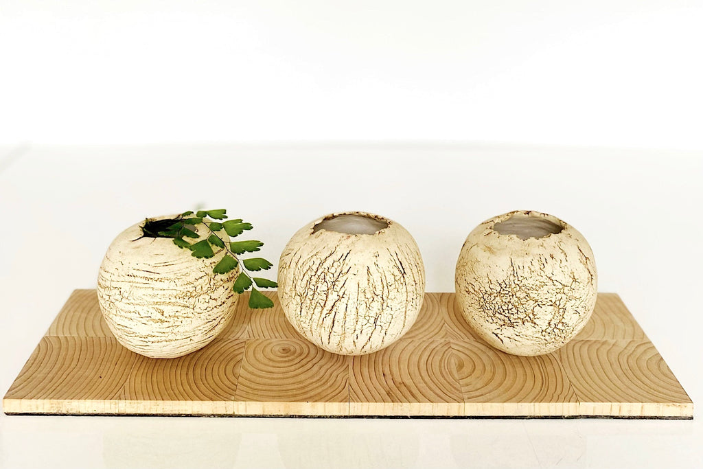 Three textured ceramic pots on a wooden board with a white background