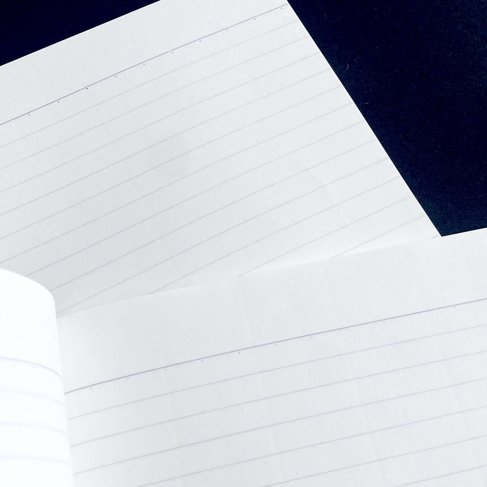 Close-up of a white notebook with lined pages on a dark blue background
