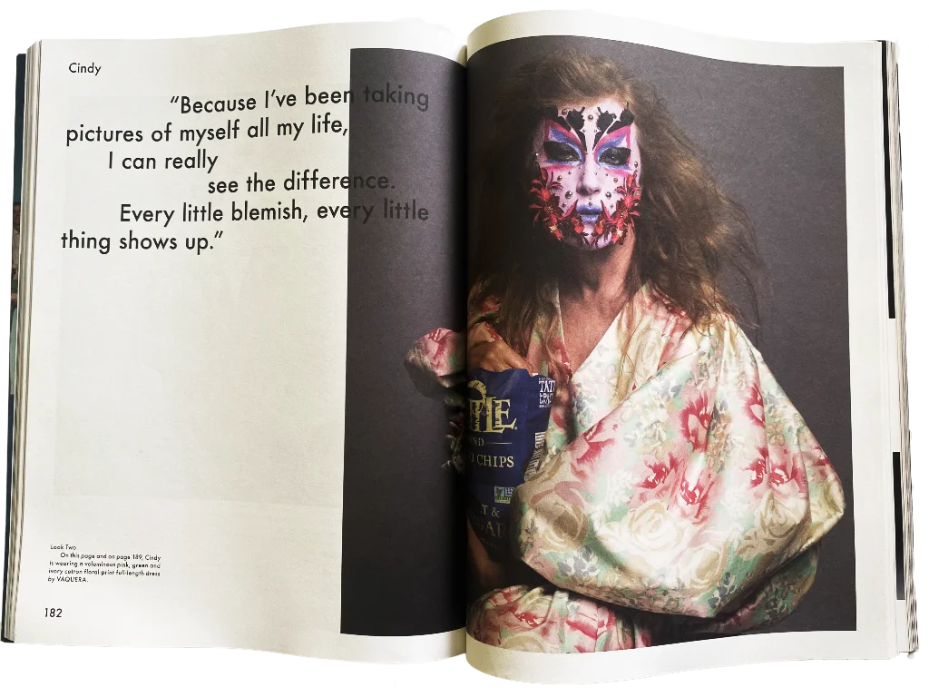 An open book or magazine spread showing a printed portrait of a woman with colorful face paint and a floral robe, alongside a quote on the left page.