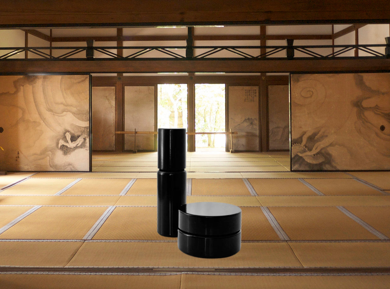 Two black cylindrical containers on a tatami mat floor with sliding doors in the background