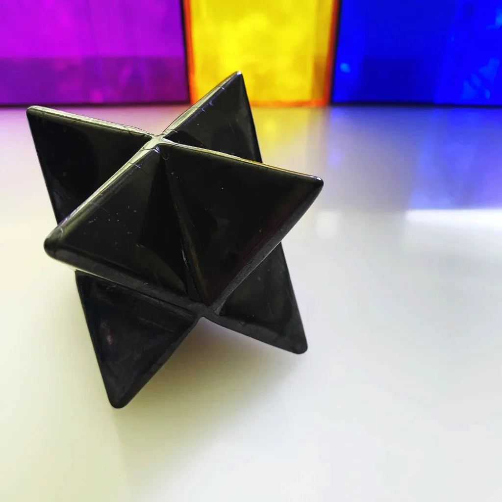 A Obsidian Star, geometric star-shaped object made of polished stone, photographed on a white surface with blurred colorful blocks in the background.