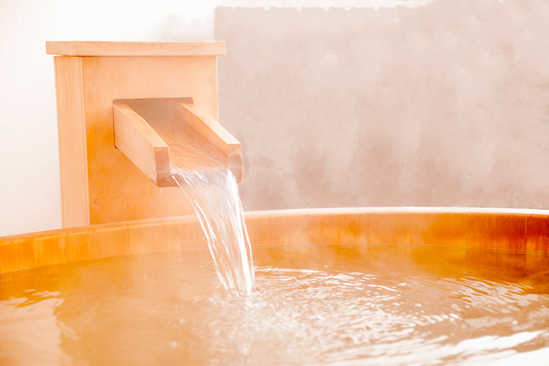 Hot tub with water flowing from a faucet, surrounded by steam.