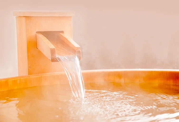 Hinoki bathtub and wood faucet pouring water into a bathtub with a warm, beige background
